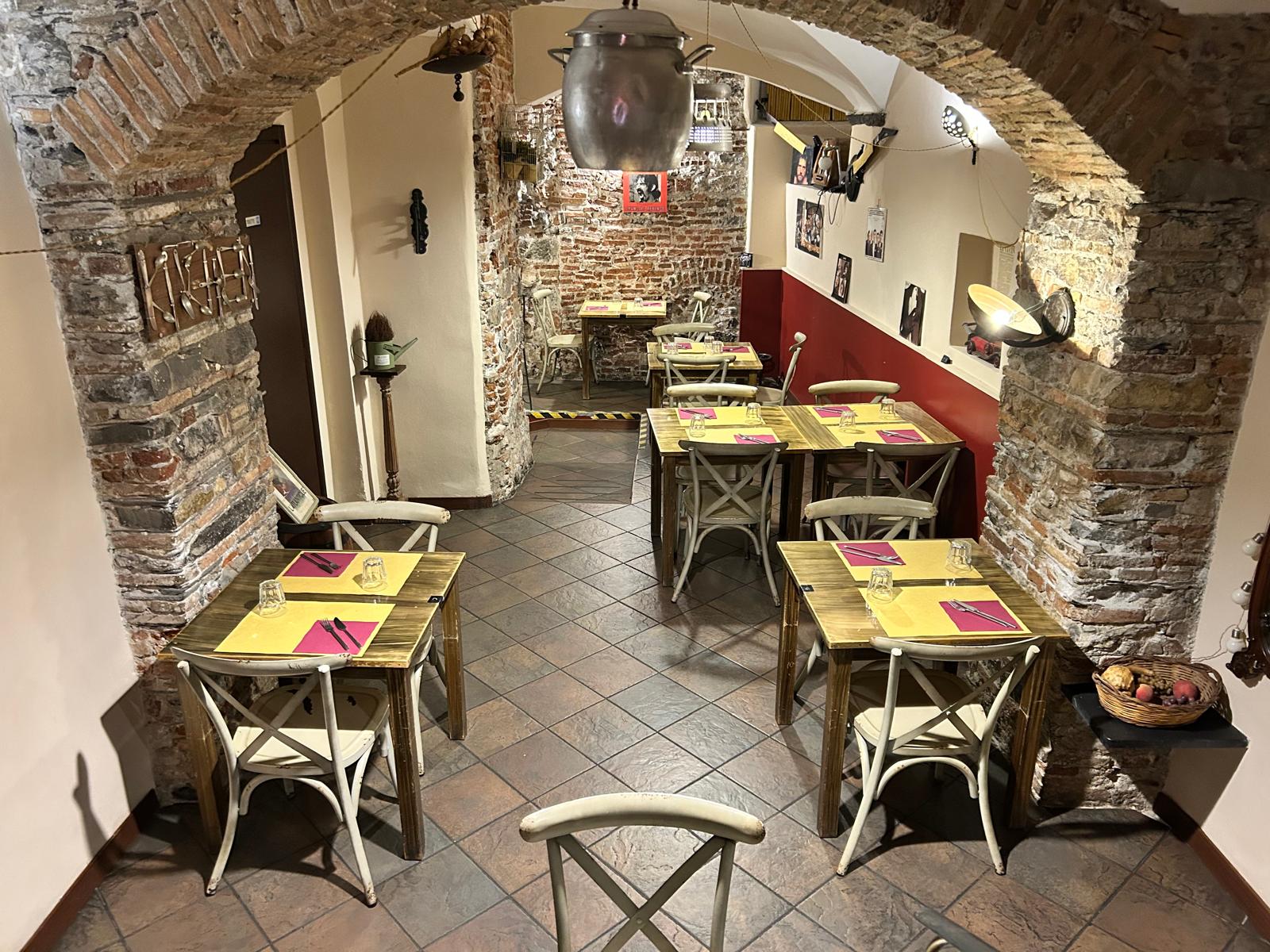 Sala di Soul Kitchen a Genova con archi in mattoni, tavoli in legno e tovagliette gialle