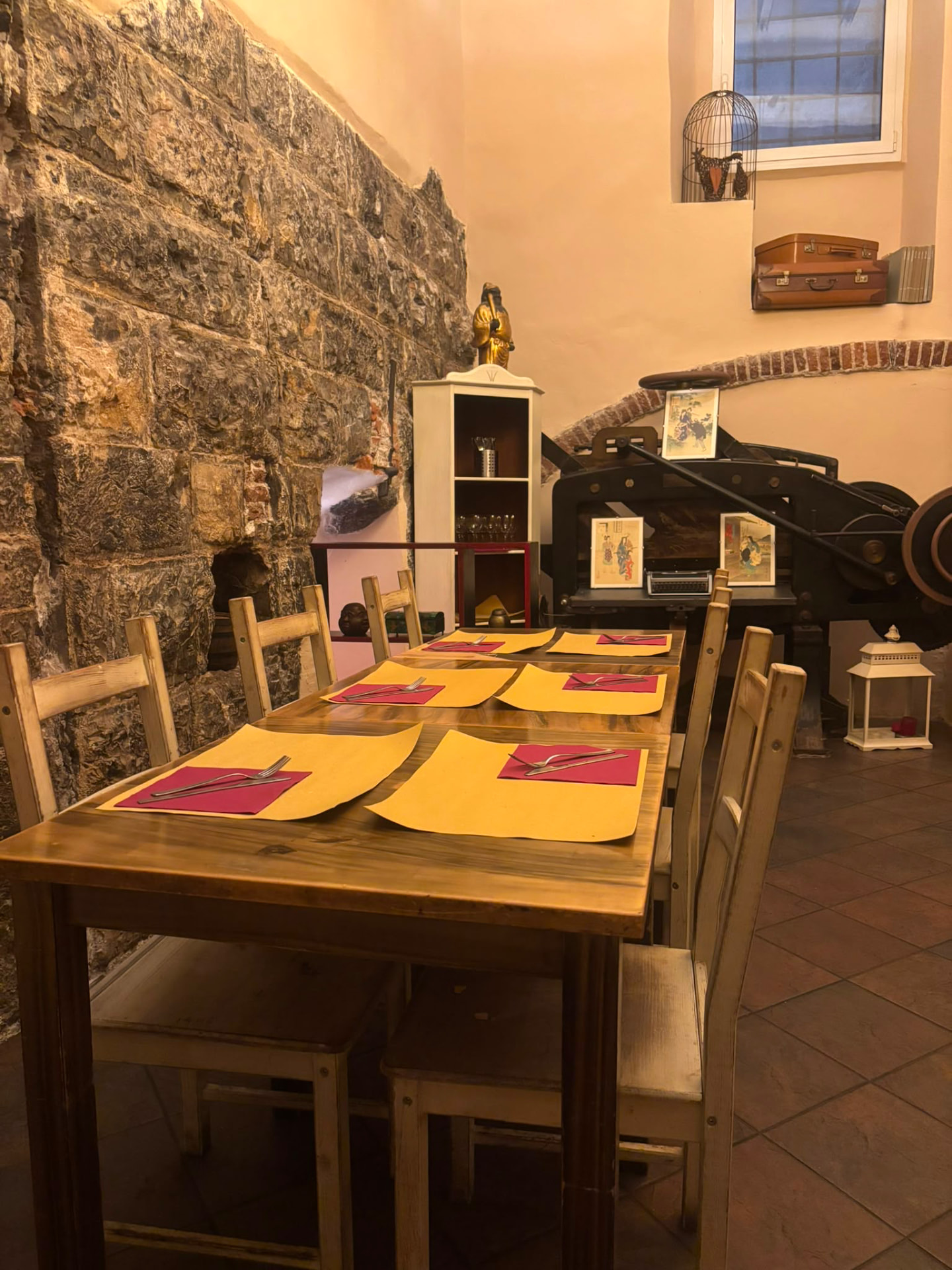 Tavolata apparecchiata con tovagliette gialle accanto a un antico torchio nella sala di Soul Kitchen