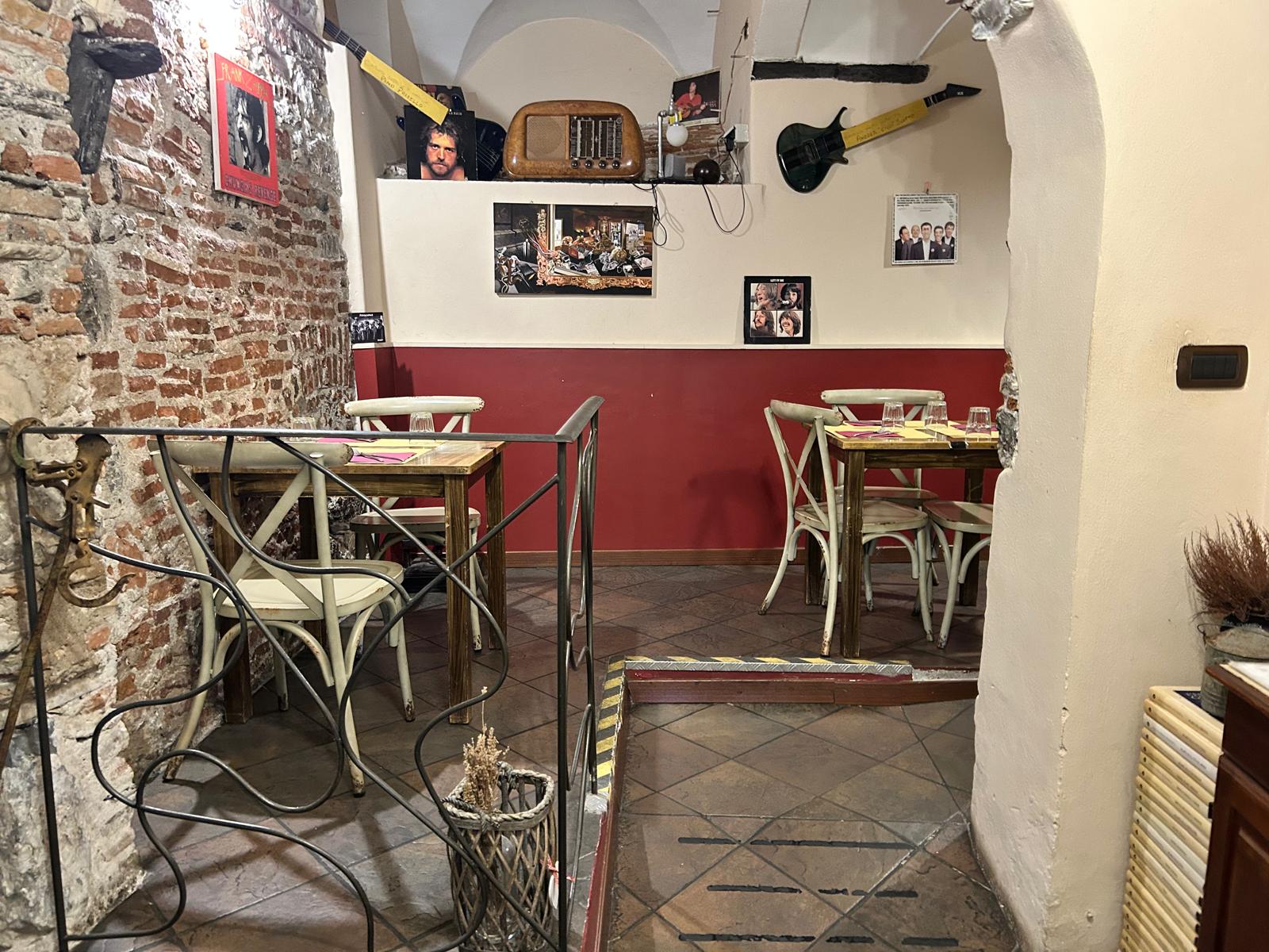 Sala con parete rossa, muri in mattoni e chitarre appese nel locale di Soul Kitchen a Genova